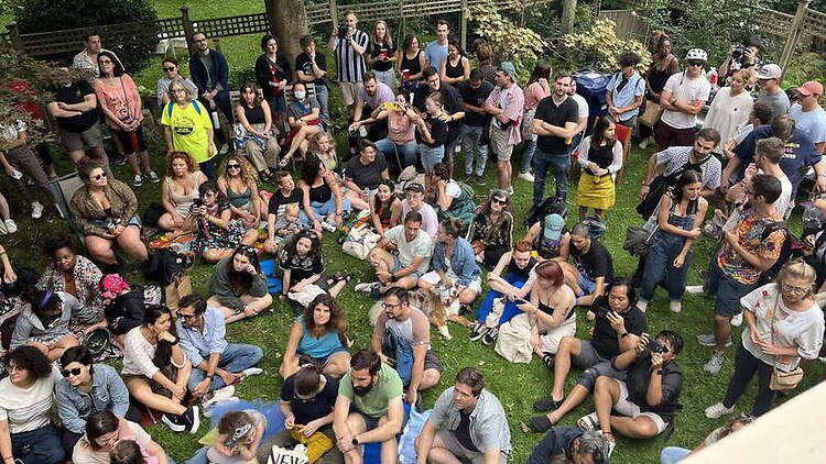 A wide shot of people gathering on a lawn at an outdoor community event. A wide shot of people gathering on a lawn at an outdoor community event.