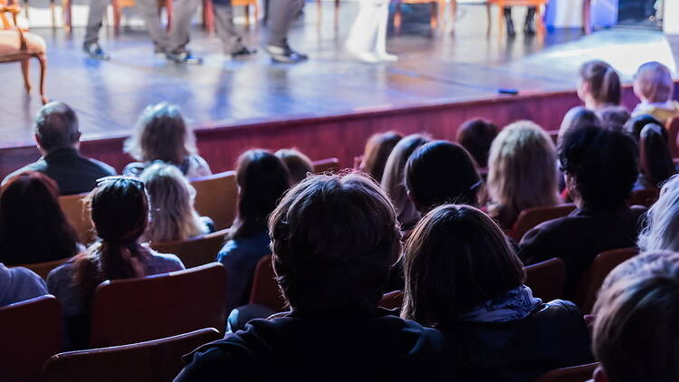 A wide shot of an audience watching a live performance in a theater. A wide shot of an audience watching a live performance in a theater.