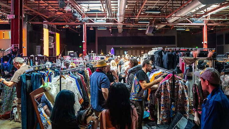 A wide shot of shoppers browsing clothing racks at an indoor market. A wide shot of shoppers browsing clothing racks at an indoor market.