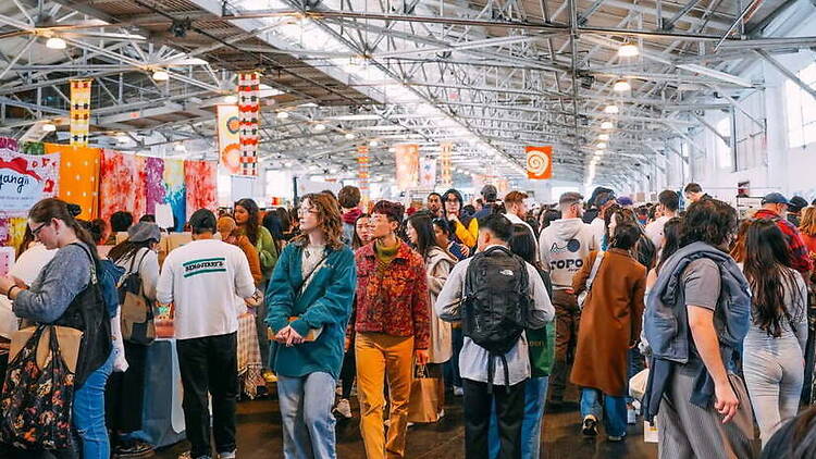 A wide shot of attendees browsing vendor booths at an indoor market. A wide shot of attendees browsing vendor booths at an indoor market.