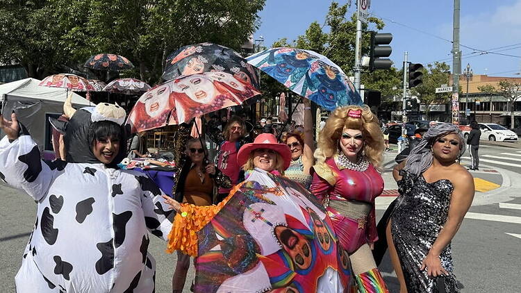 A wide shot of people in colorful costumes posing at an outdoor street festival