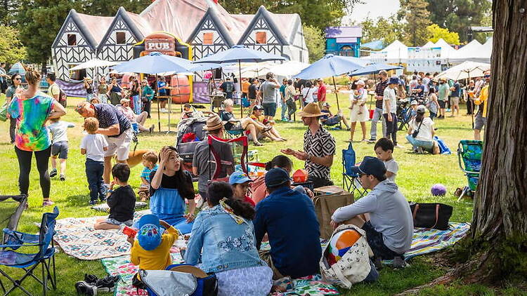 A wide shot of people relaxing and gathering at an outdoor festival A wide shot of people relaxing and gathering at an outdoor festival