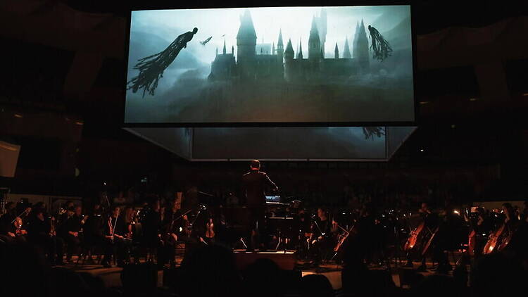 Wide view of orchestra performing beneath a large screen in a concert hall. Wide view of orchestra performing beneath a large screen in a concert hall.