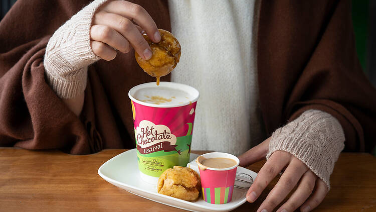 A person dipping a syrup dumpling into a hot chocolate.