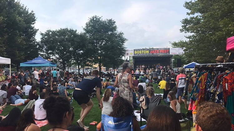 A wide shot of people watching a performance at an outdoor festival A wide shot of people watching a performance at an outdoor festival