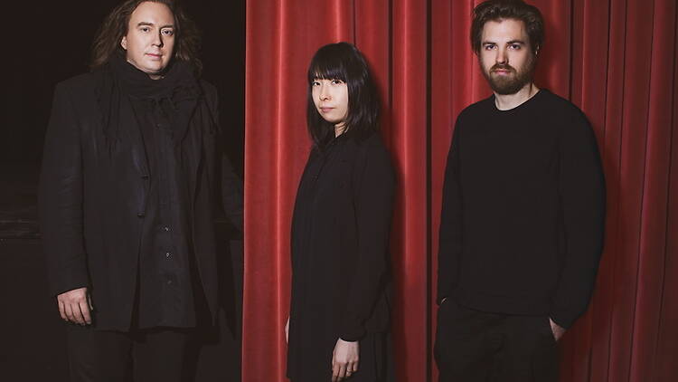 Three people posing in front of a red curtain