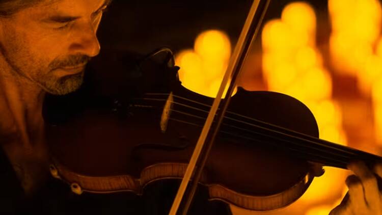 A close-up of a person playing a violin under warm stage lighting A close-up of a person playing a violin under warm stage lighting