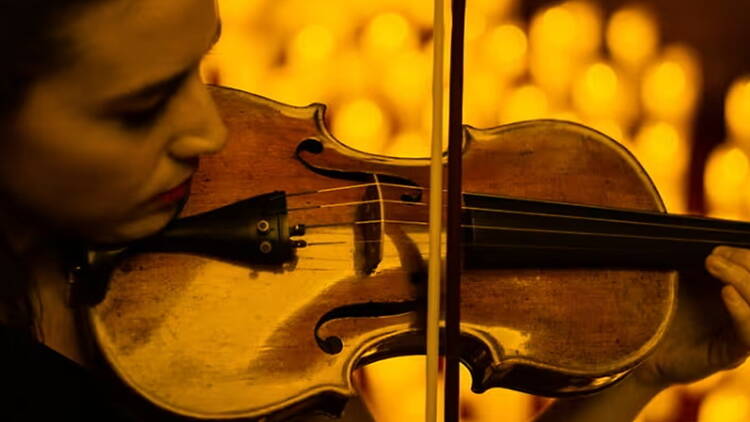 A close-up of a person playing a violin under warm stage lighting