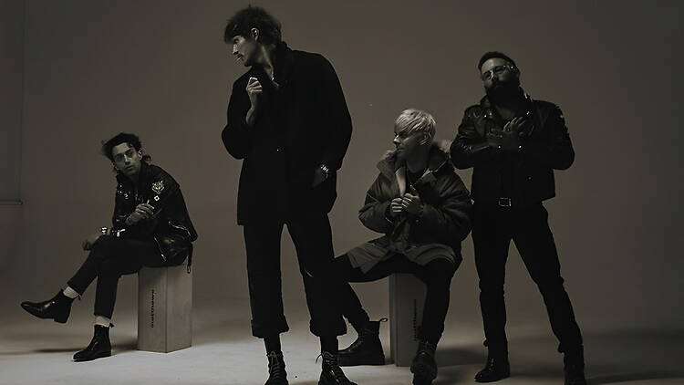 A wide shot of four band members posing in a studio with a plain background. A wide shot of four band members posing in a studio with a plain background.