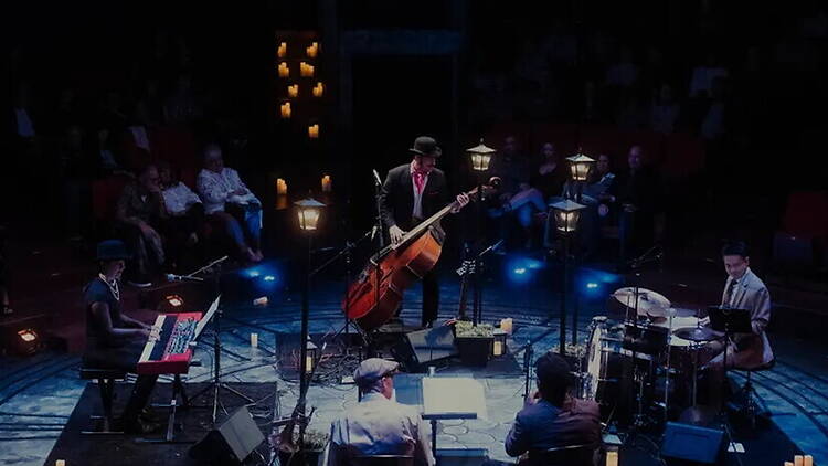 A wide shot of a jazz band performing on a candlelit stage in front of an audience.