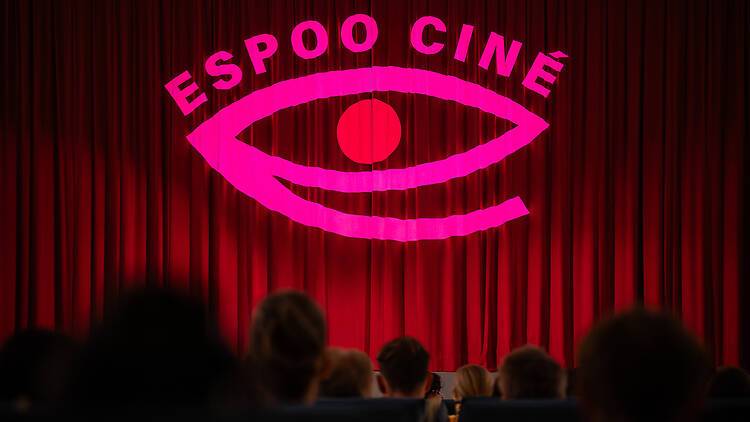 Espoo Ciné elokuvafestarin logo heijastuu elokuvateatterin punaiseen esirippuun Espoo Ciné elokuvafestarin logo heijastuu elokuvateatterin punaiseen esirippuun