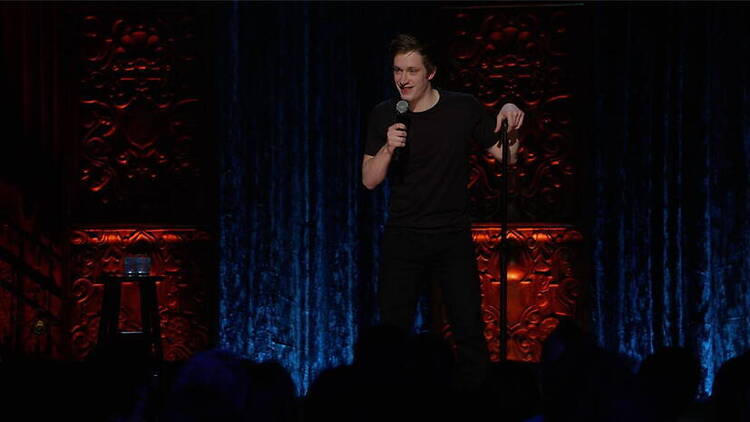 A wide shot of a comedian performing with a microphone on a theater stage. A wide shot of a comedian performing with a microphone on a theater stage.
