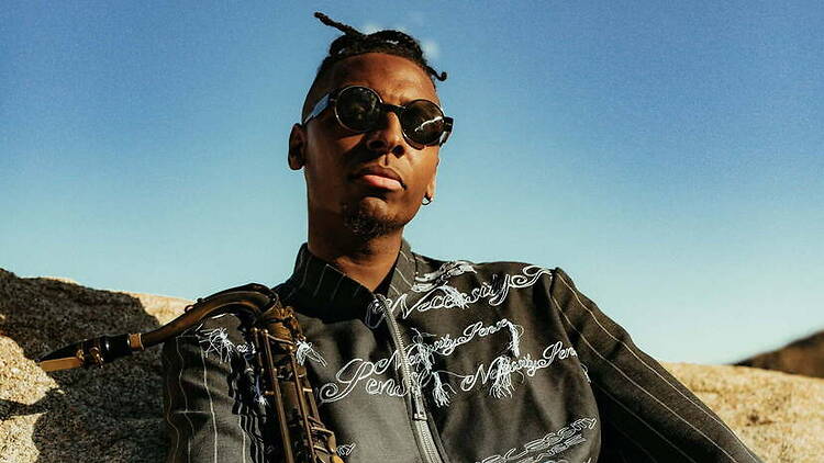 A close-up of a person holding a saxophone outdoors in a desert landscape. A close-up of a person holding a saxophone outdoors in a desert landscape.