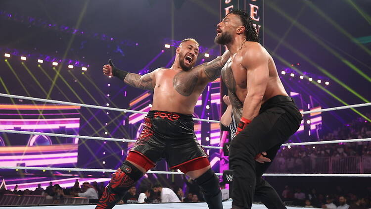 A wide shot of two wrestlers competing in a wrestling ring during a live event. A wide shot of two wrestlers competing in a wrestling ring during a live event.