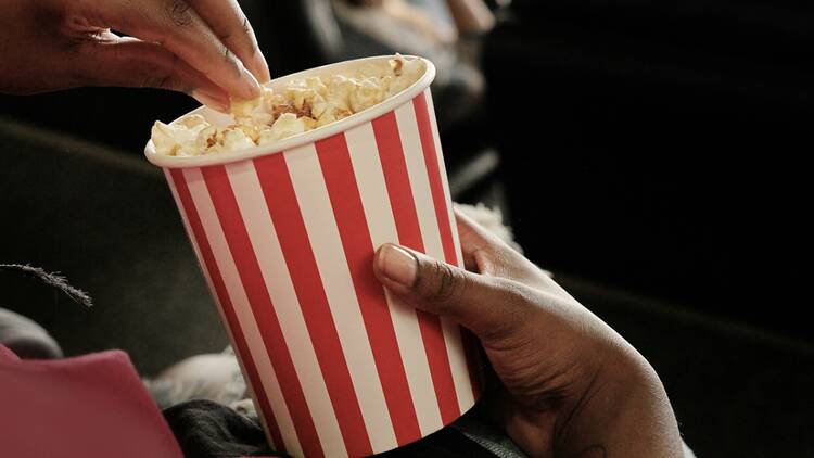 A close-up of hands sharing popcorn in a movie theater. A close-up of hands sharing popcorn in a movie theater.