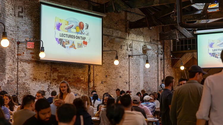 A wide shot of people attending a lecture in an indoor event space.