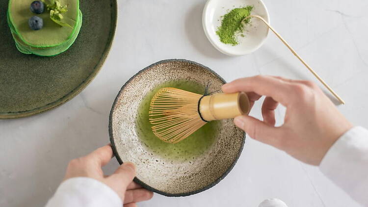 A close-up of hands whisking matcha tea in a bowl on a countertop.