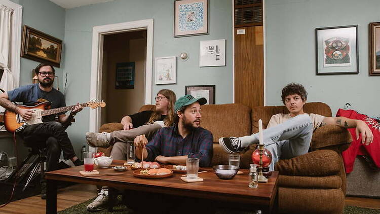 A wide shot of people relaxing together in a living room while one person plays guitar. A wide shot of people relaxing together in a living room while one person plays guitar.