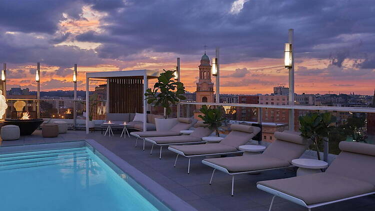 A wide shot of a rooftop pool overlooking a city skyline at sunset. A wide shot of a rooftop pool overlooking a city skyline at sunset.