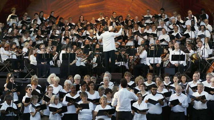A wide shot of a choir and orchestra performing on stage in a concert hall. A wide shot of a choir and orchestra performing on stage in a concert hall.