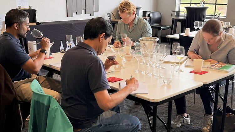A wide shot of people tasting wine at an indoor workshop. A wide shot of people tasting wine at an indoor workshop.