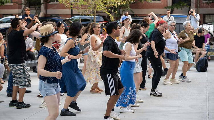 A wide shot of people dancing together at an outdoor community event. A wide shot of people dancing together at an outdoor community event.