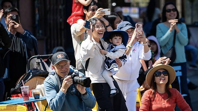 A wide shot of spectators watching and taking photos at an outdoor event.