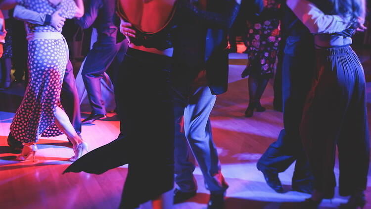 A close-up of couples dancing together on a dance floor under colorful stage lights.
