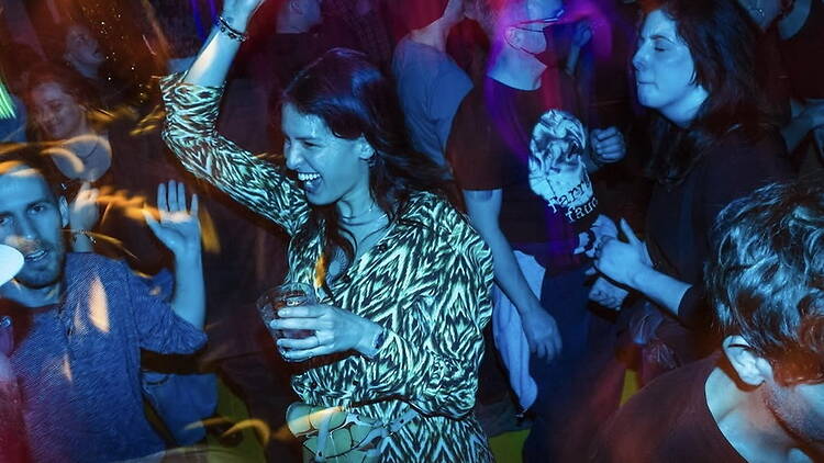 A close-up of people dancing and holding drinks at a nightclub.