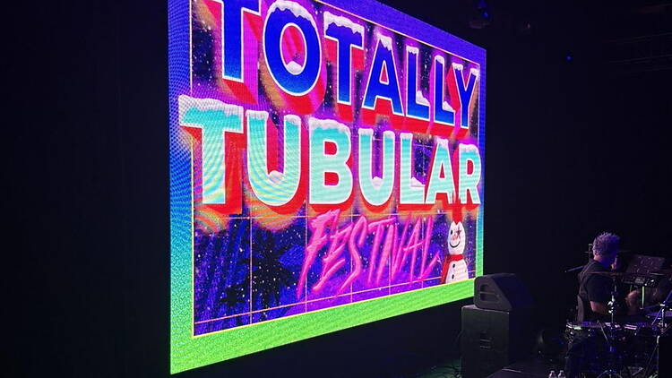 A wide shot of a festival sign displayed on a stage beside a musician. A wide shot of a festival sign displayed on a stage beside a musician.