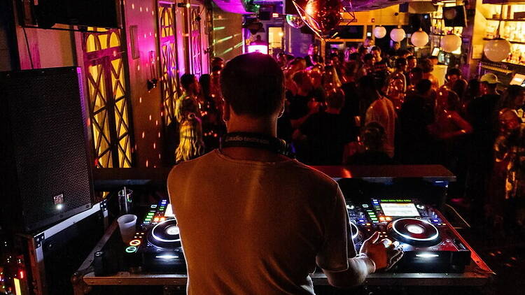 A wide shot of a DJ performing for a crowd in a nightclub. A wide shot of a DJ performing for a crowd in a nightclub.