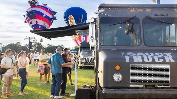 Wide shot of people waiting at a food truck during an outdoor festival. Wide shot of people waiting at a food truck during an outdoor festival.