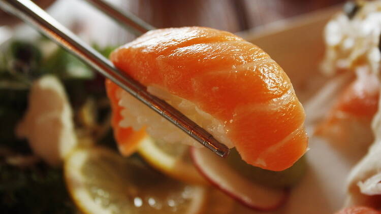 Close-up of salmon sushi held with chopsticks over a dining table. Close-up of salmon sushi held with chopsticks over a dining table.