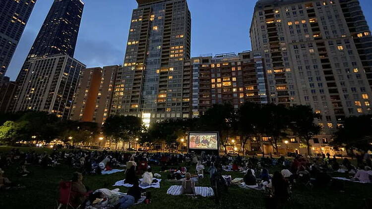 Wide shot of people watching an outdoor movie in a city park at night. Wide shot of people watching an outdoor movie in a city park at night.