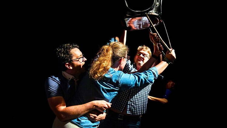 Close-up of three people lifting a chair during a stage performance. Close-up of three people lifting a chair during a stage performance.