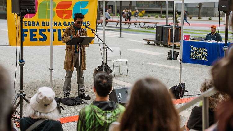 A wide shot of a person speaking to an audience at an outdoor festival. A wide shot of a person speaking to an audience at an outdoor festival.