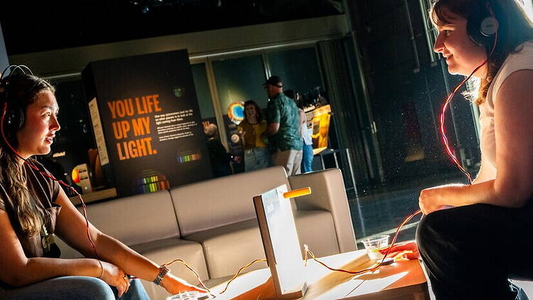 A wide shot of two people wearing headphones at an interactive exhibit in a museum