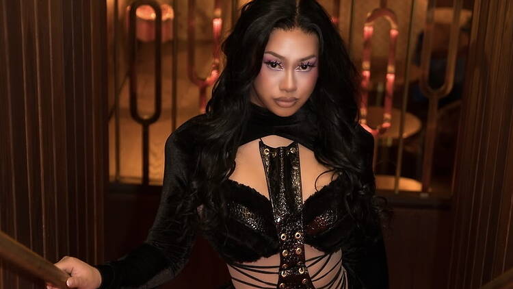 Close-up of a person posing in a black outfit inside a warmly lit venue. Close-up of a person posing in a black outfit inside a warmly lit venue.