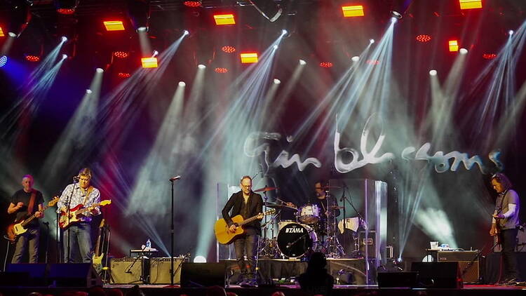 Wide shot of a band performing on a brightly lit concert stage before an audience. Wide shot of a band performing on a brightly lit concert stage before an audience.