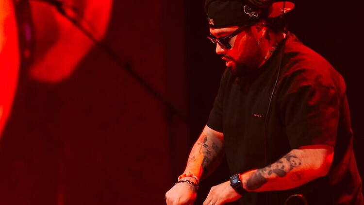 Close-up of a DJ mixing music on stage under red lights. Close-up of a DJ mixing music on stage under red lights.