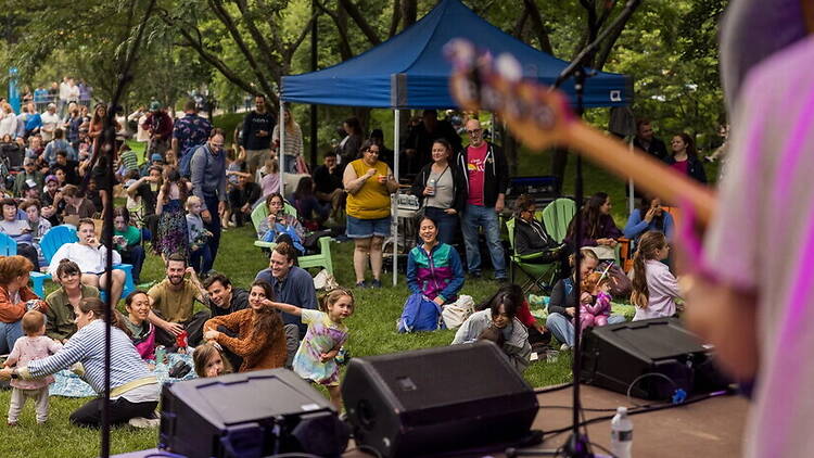A wide shot of people watching a performance in a park A wide shot of people watching a performance in a park