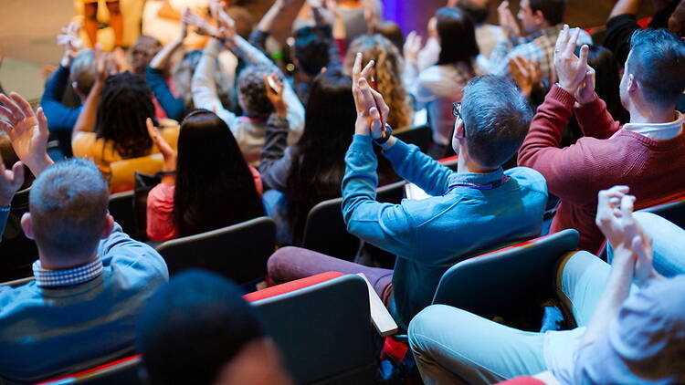 A wide shot of people applauding in a theatre A wide shot of people applauding in a theatre