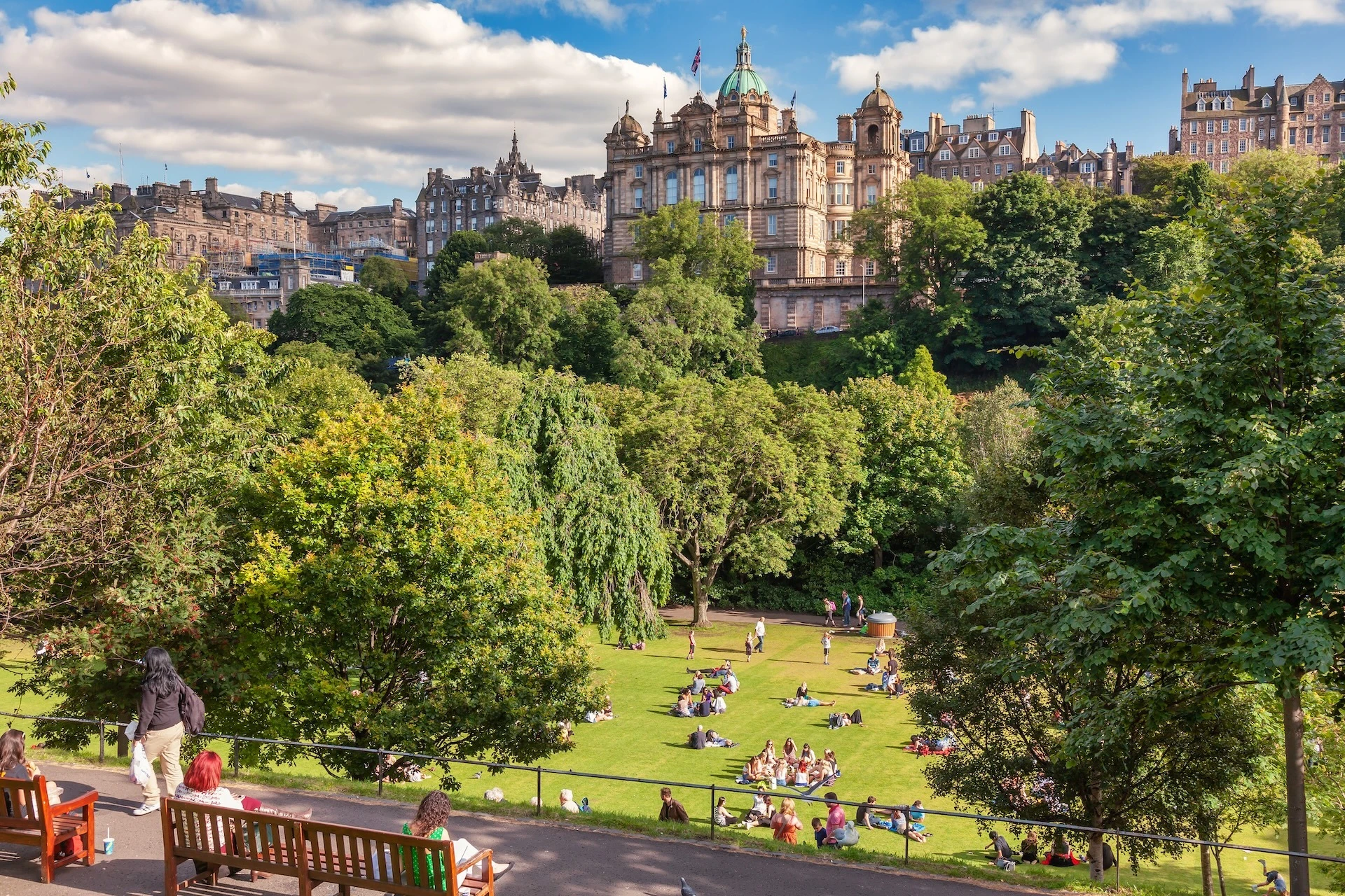 Locals and tourists enjoy warm sunny summer day relaxing and picnicking at the Princes Street Gardens a famous public park
