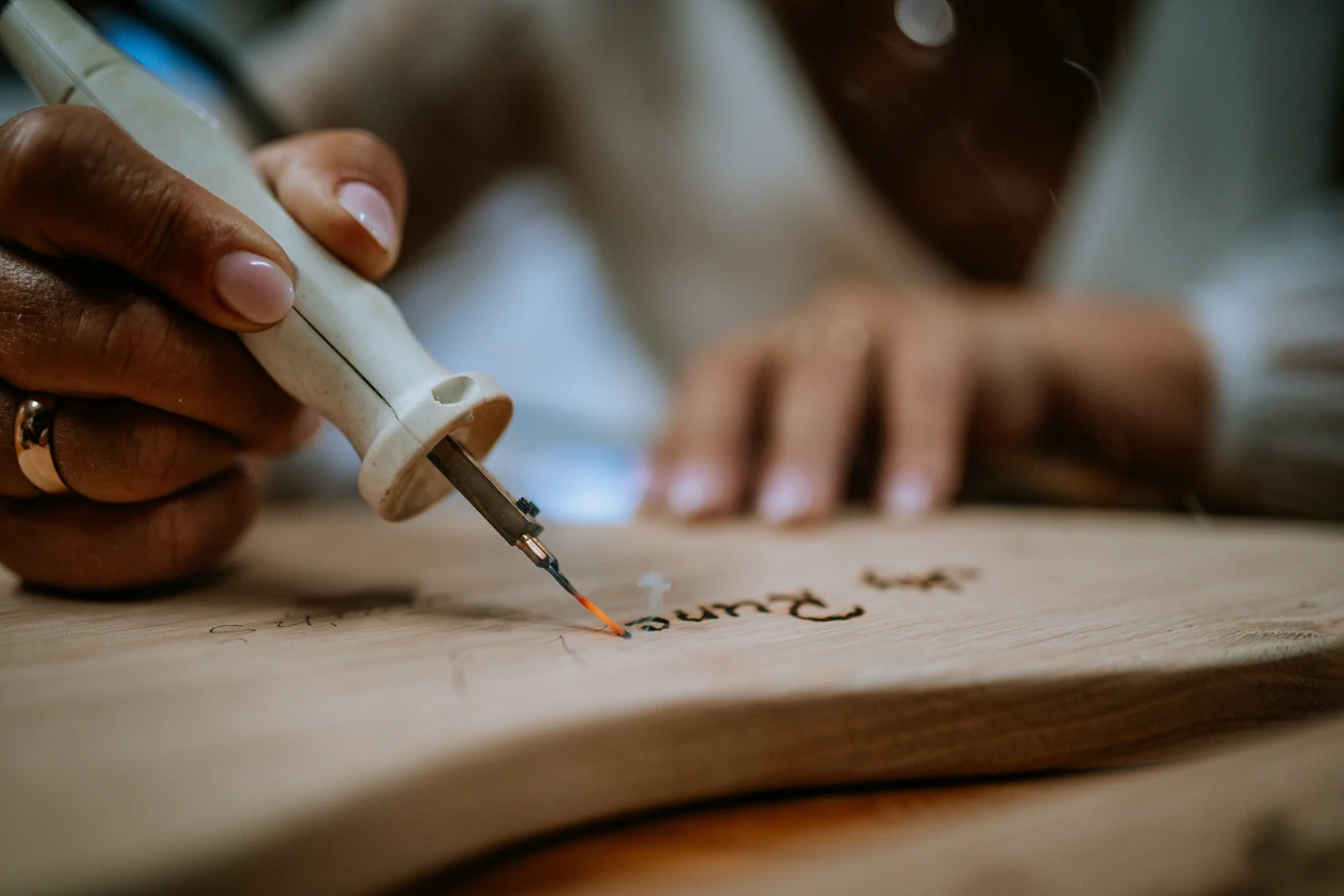 Female artisan focuses on wood burning technique, crafting detailed designs on a wooden piece in a bright workshop environment