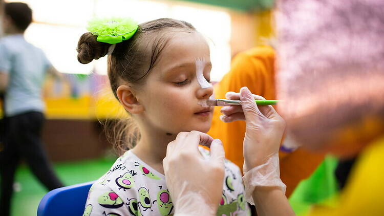 A close-up of a child having face paint applied at an indoor event. A close-up of a child having face paint applied at an indoor event.