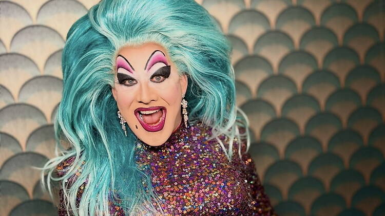 A close-up of a performer smiling at the camera against a patterned backdrop A close-up of a performer smiling at the camera against a patterned backdrop