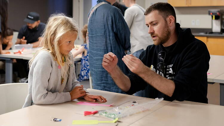 A close-up of an adult showing a child a craft activity at a workshop. A close-up of an adult showing a child a craft activity at a workshop.
