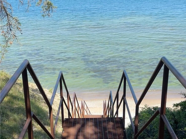 Södra Hällarna nature reserve, popular stop just outside Visby. Metal staircase leading down a grassy cliff to a sandy shore and clear turquoise water at Södra hällarna in Gotland, Sweden.