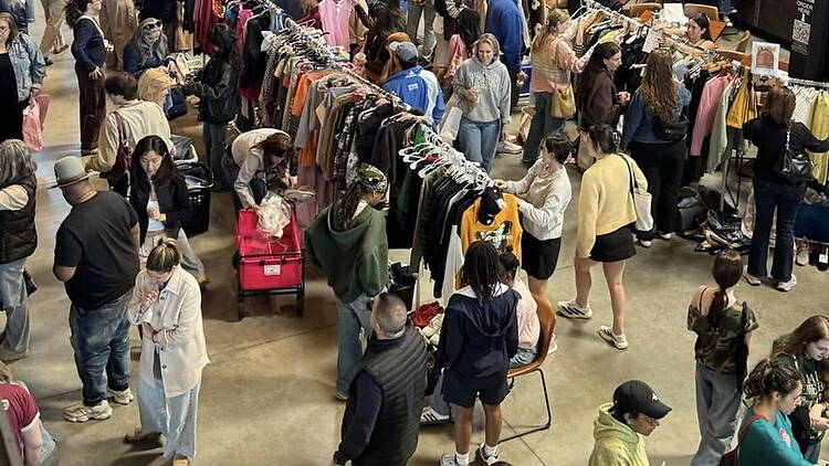 Wide shot of shoppers browsing clothing racks at an indoor market.
