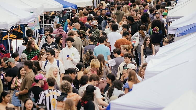 Wide shot of a crowd browsing vendor booths at an outdoor street market.